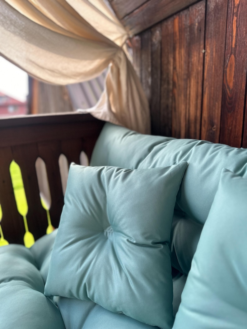 May include: A light blue cushion with a button detail and a white sheer curtain in the background.