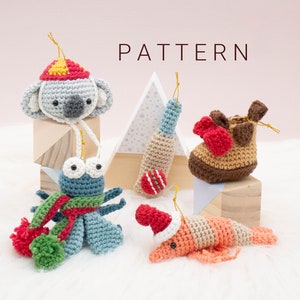 Könnte beinhalten: Fünf gehäkelte Ornamente, darunter ein Koala mit einem rot-gelben Hut, ein Cricket-Schläger, ein Stiefel, eine Garnele mit einem roten Weihnachtsmann-Hut und ein blauer Käfer mit einem rot-grünen Schal.