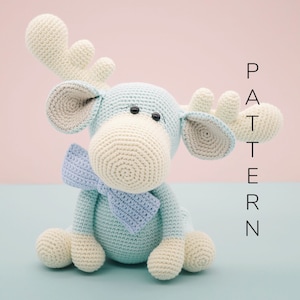 May include: A crocheted blue and white moose toy with a blue bow tie. The toy is sitting on a light blue surface. PATTERN