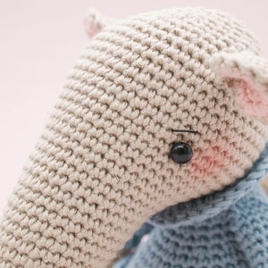 K&ouml;nnte beinhalten: Nahaufnahme eines geh&auml;kelten Stofftieres mit beigefarbenem K&ouml;rper, rosa Ohren und schwarzen Augen. Das Tier tr&auml;gt einen blauen H&auml;kel-Schal.