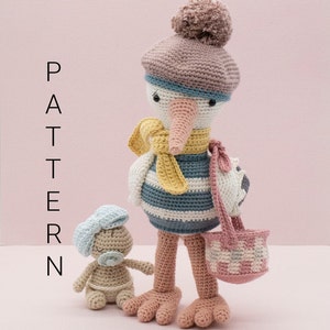 Puede incluir: Una cigüeña de crochet con un cuerpo a rayas azul y blanco, un sombrero rosa y una bufanda amarilla, llevando una cesta rosa y blanca. Una pequeña muñeca de crochet con un lazo azul está de pie junto a la cigüeña.