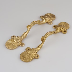 May include: Two gold-toned door handles featuring a decorative elephant head design. The handles are curved and have a circular base.