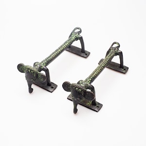 May include: A pair of antique bronze door handles featuring an elephant head design. The handles are dark bronze with green detailing. The elephant heads are at the base of the handles. The handles are rectangular and have a textured design.