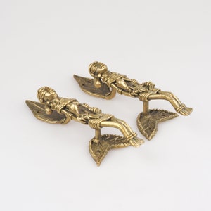 May include: A pair of gold-toned metal door handles with a leaf design and a figure of a person lying down.