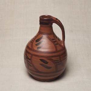 May include: A round, terracotta-coloured ceramic pitcher with a narrow neck and a single handle. The surface features dark brown horizontal bands and repeating leaf-like brushstroke patterns encircling the body of the vessel.