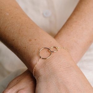 A close-up image of a person's wrist wearing a gold-colored bracelet with two circular rings.