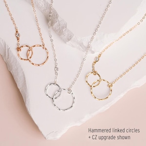 three necklaces with different designs, including hammered linked circles and a CZ upgrade shown.