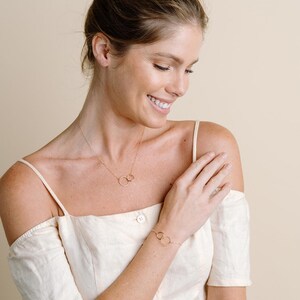 A woman wearing a white off-the-shoulder top and a bracelet is smiling and looking down at her hand.
