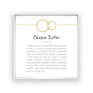 May include: A gold-toned necklace featuring two interlocking hammered circles on a delicate chain, presented on a white card with the text Chosen Sister and a printed message expressing gratitude and friendship for a special person.