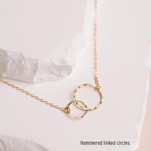 A delicate gold necklace with two intertwined rings, resting on a white stone surface.