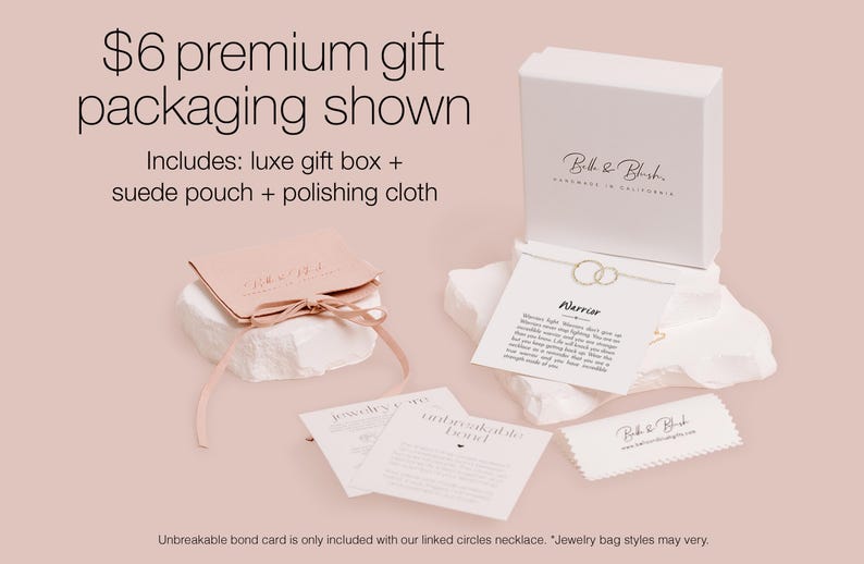 a premium gift packaging for a necklace, including a luxury gift box, a suede pouch, and a polishing cloth. The packaging is presented on a light pink background, and there is a note indicating that an Unbreakable Bond card is included with the necklace.