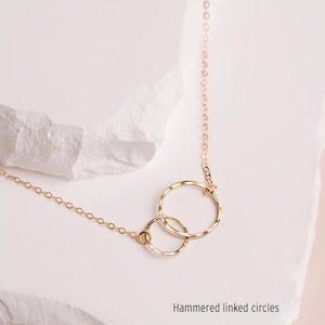 A delicate gold necklace with two intertwined rings, resting on a white stone surface.