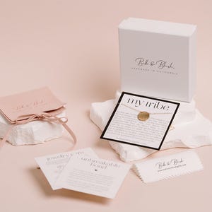 a collection of jewelry and accessories, including a necklace, a box, and some informational cards, all set against a light pink background.