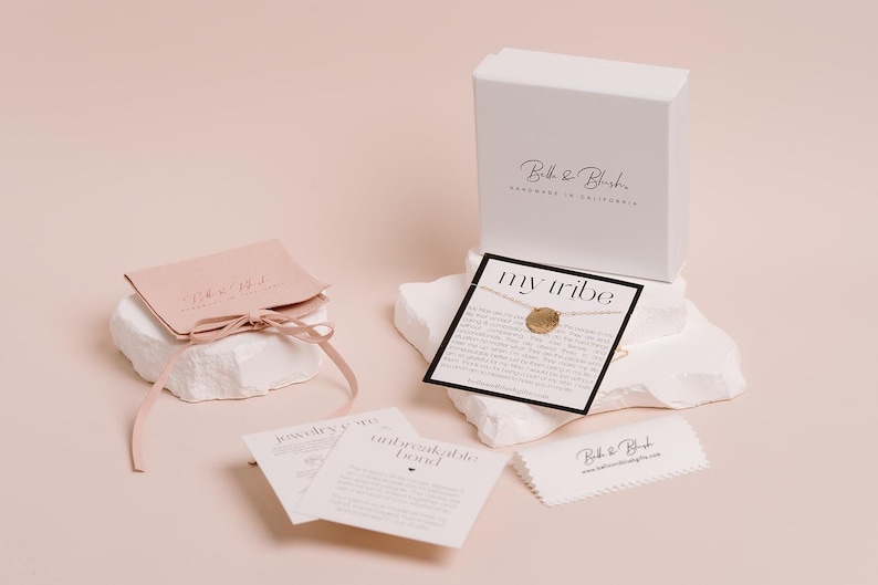 a collection of jewelry and accessories, including a necklace, a box, and some informational cards, all set against a light pink background.