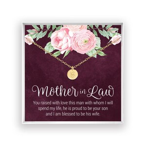 Könnte beinhalten: Eine goldfarbene Halskette mit einem kleinen runden Anhänger, der den Buchstaben B zeigt. Die Kette ist auf einer quadratischen Karte mit dunkelviolettem Hintergrund, rosa Blumenillustrationen sowie dem Text Mother in Law und einem Text.
