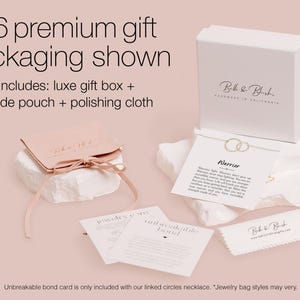 a premium gift packaging for a necklace, including a luxury gift box, a suede pouch, and a polishing cloth. The packaging is presented on a light pink background, and there is a note indicating that an Unbreakable Bond card is included with the necklace.