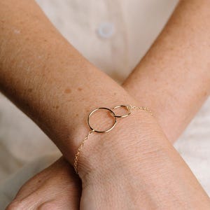 A close-up image of a person's wrist wearing a gold-colored bracelet with two circular rings.