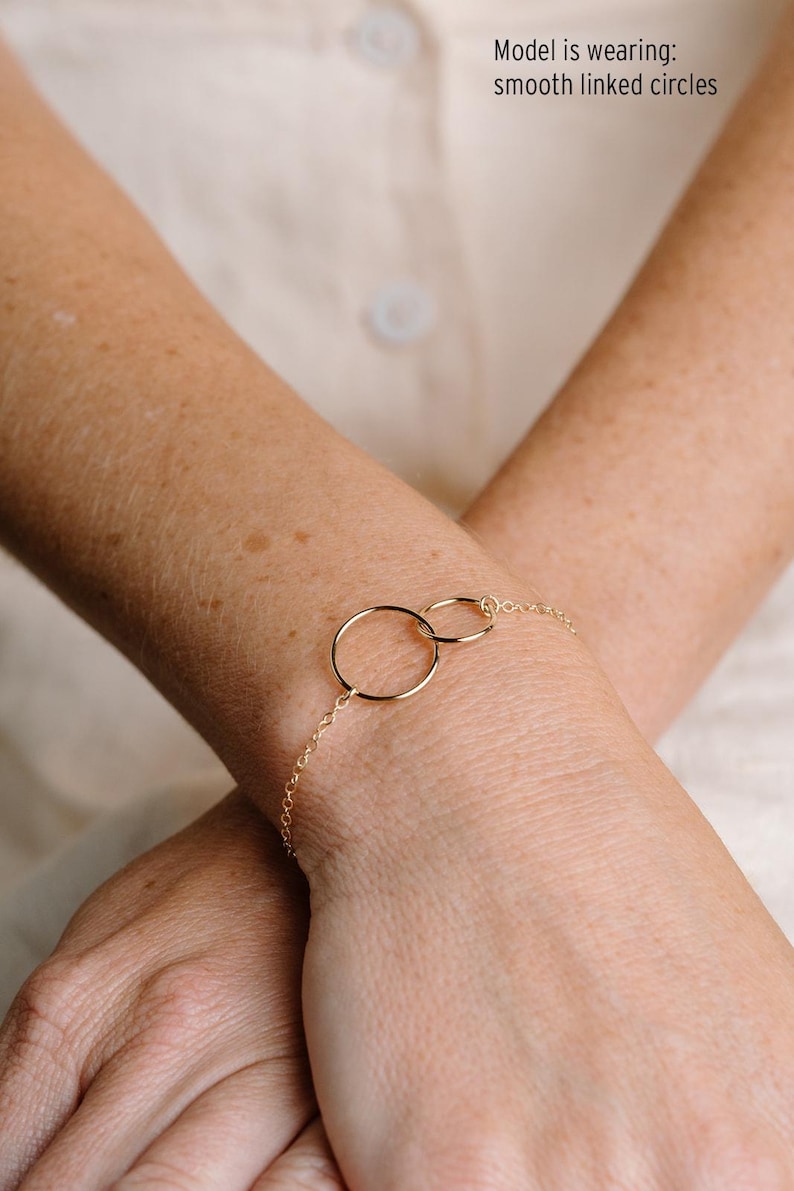 A close-up image of a person's wrist wearing a gold-colored bracelet with two circular rings.