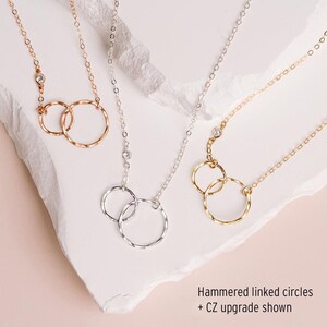 three necklaces with different designs, including hammered linked circles and a CZ upgrade shown.