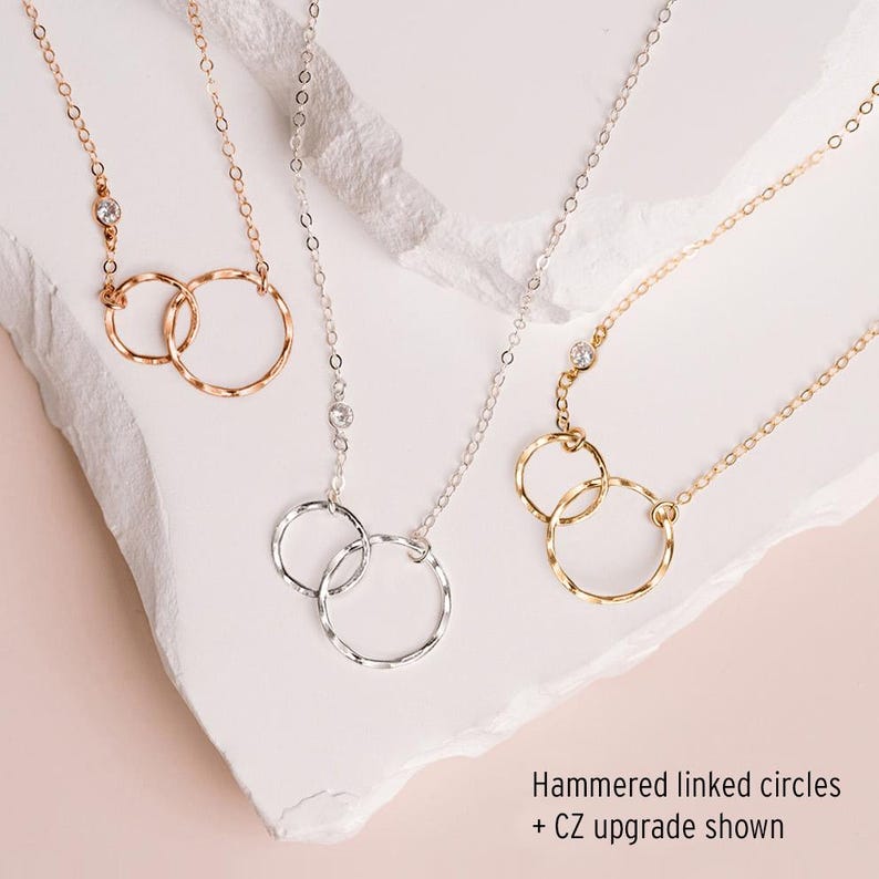 three necklaces with different designs, including hammered linked circles and a CZ upgrade shown.