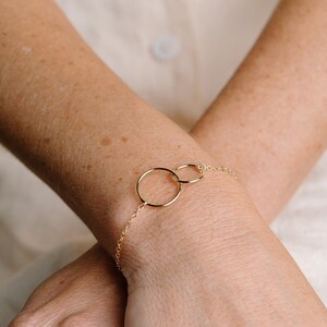 A close-up image of a person's wrist wearing a gold-colored bracelet with two circular rings.
