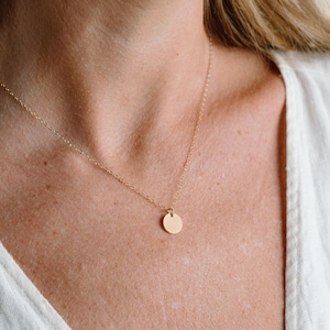 A close-up view of a woman's neck and chest area, featuring a delicate gold necklace with a small round pendant.