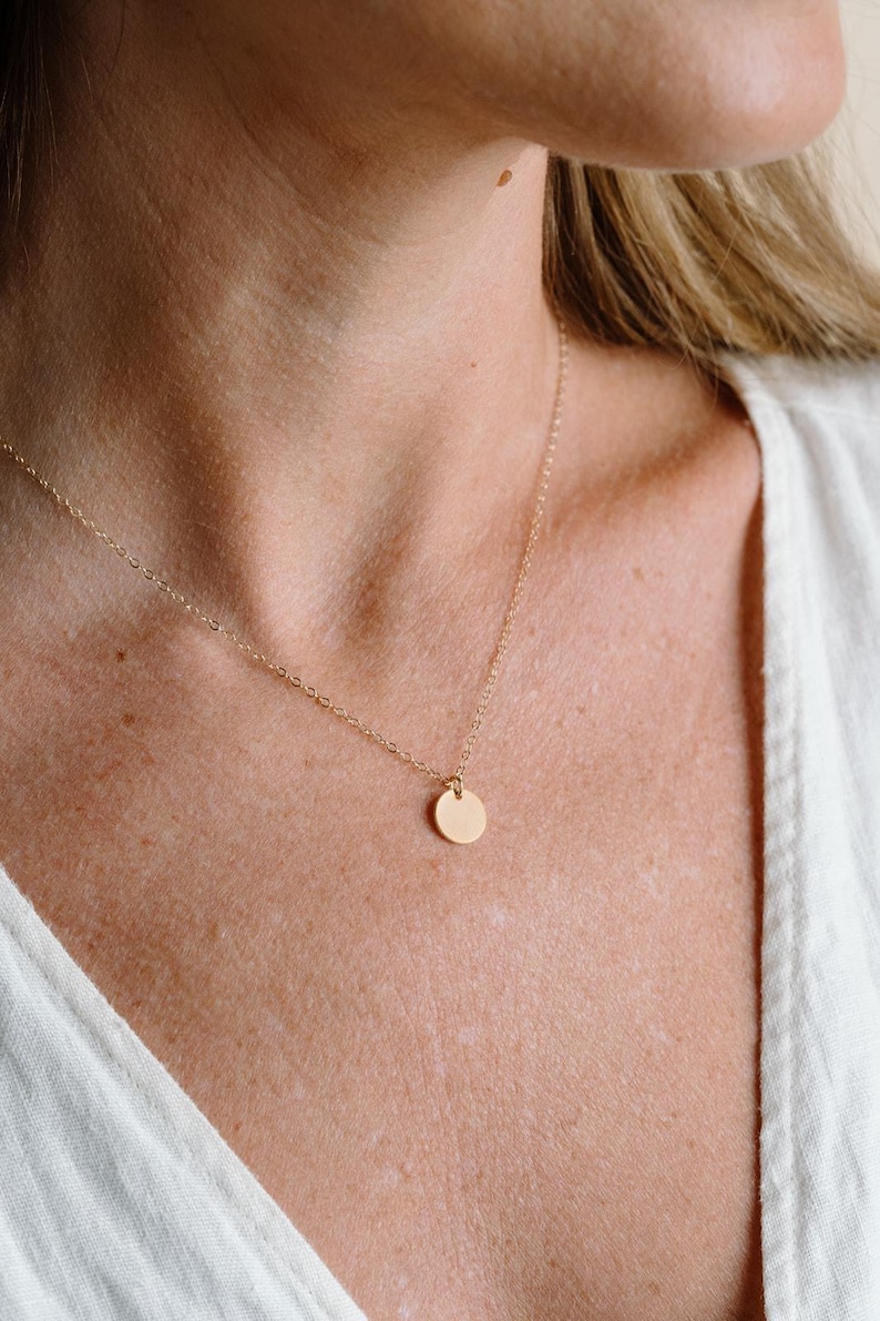 A close-up view of a woman's neck and chest area, featuring a delicate gold necklace with a small round pendant.