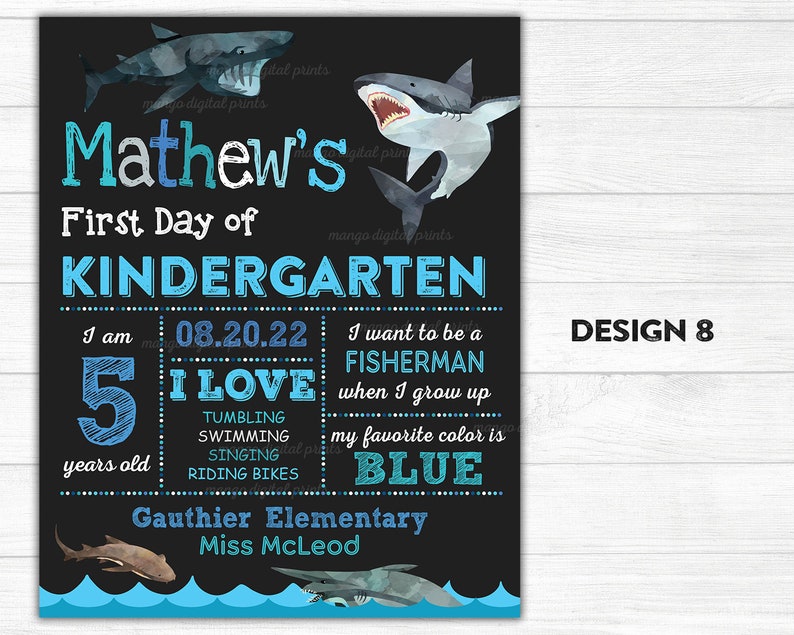 Puede incluir: Un cartel de estilo pizarra negra con un dise&ntilde;o azul y blanco que presenta un tibur&oacute;n y el texto "Mathew's First Day of Kindergarten". El cartel tambi&eacute;n incluye la fecha "08.20.22", la edad "5 a&ntilde;os" y la frase "Me encanta hacer volteretas, nadar, cantar, andar en bicicleta". El cartel tambi&eacute;n indica que el ni&ntilde;o quiere ser pescador cuando crezca y que su color favorito es el azul. El cartel es de la escuela primaria Gauthier y el nombre de la maestra es la se&ntilde;orita McLeod.
