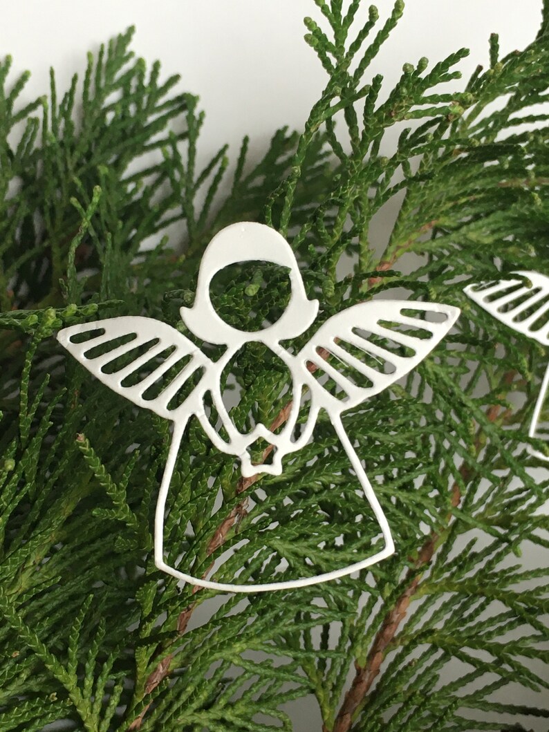 Pode incluir: Adorno de anjo branco recortado com asas e halo. O adorno &eacute; feito de metal e tem um design delicado. &Eacute; perfeito para adicionar um toque de eleg&acirc;ncia &agrave; sua &aacute;rvore de Natal.