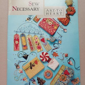 May include: A light blue book cover with the text "Sew Necessary" and "Art-to-Heart". The cover features various handmade fabric items, including bookmarks, purses, and ornaments in various colors and patterns.
