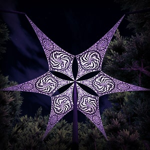 May include: A large, six-pointed star-shaped canopy made of white and black patterned fabric, suspended from a central pole against a night sky.