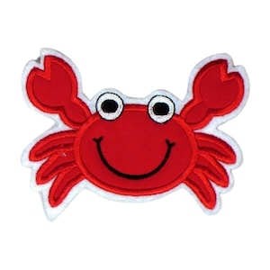 Könnte beinhalten: Rote Filz-Krabben-Applikation mit weißem Umriss und schwarzen Augen. Die Krabbe hat einen lächelnden Mund.