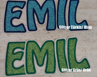 May include: Two sets of iron-on letters spelling "EMIL" in a whimsical font. The top set is turquoise blue with a dark blue outline and the bottom set is green with a dark green outline. The text "Glitter Türkis/Blau" is below the top set and "Glitter Grün/Grün" is below the bottom set.