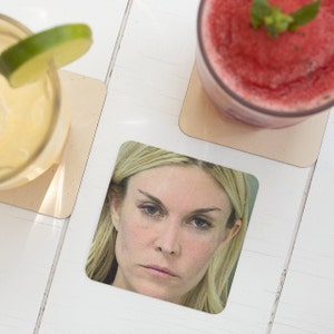 May include: A close-up of a woman's face with blonde hair. She has dark eyebrows and is looking directly at the camera. The image is printed on a square coaster.