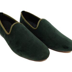 May include: A pair of dark green velvet loafers with a light green trim around the edge.