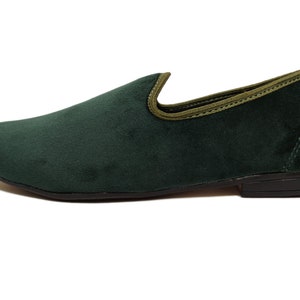 May include: A pair of dark green velvet loafers with a light green trim around the top edge. The loafers have a black rubber sole.