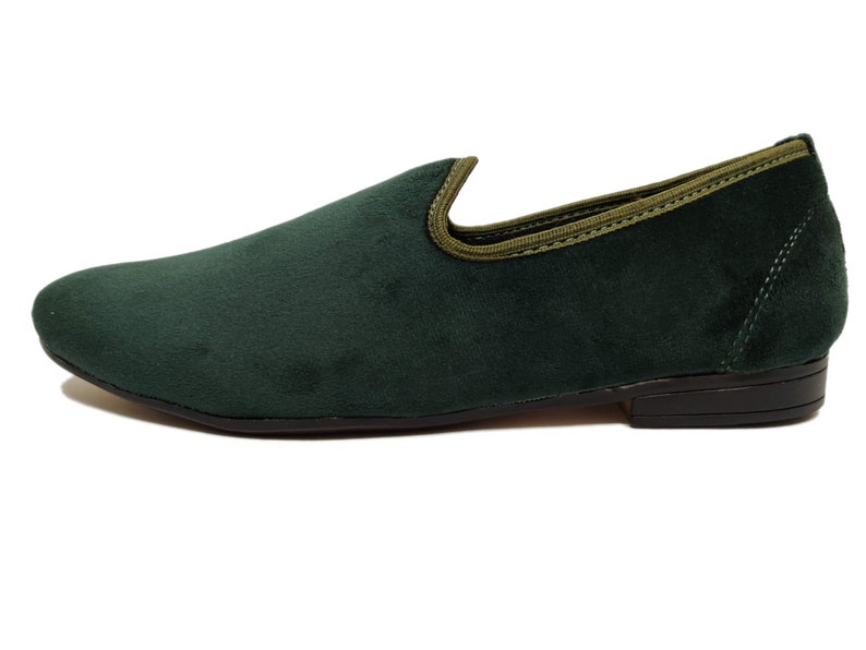 May include: A pair of dark green velvet loafers with a light green trim around the top edge. The loafers have a black rubber sole.