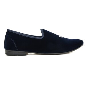 May include: A navy blue velvet slipper with a rounded toe and a low heel. The shoe features a white embroidered design on the upper. The shoe has a dark sole and a contrasting trim around the opening.