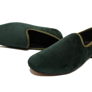 May include: A pair of dark green velvet loafers with a light green trim around the edge. The loafers have a pointed toe and a low heel.