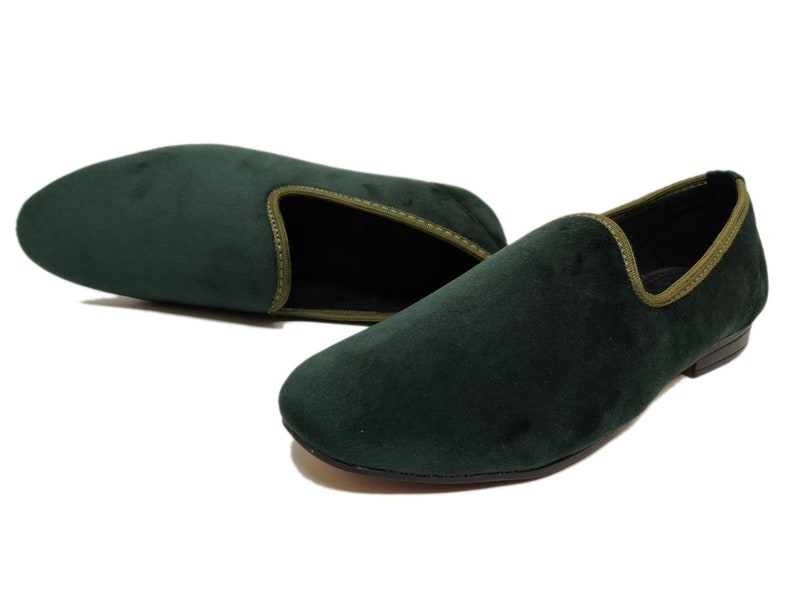 May include: A pair of dark green velvet loafers with a light green trim around the edge. The loafers have a pointed toe and a low heel.