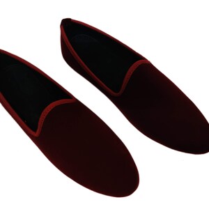 May include: A pair of burgundy velvet loafers. These slip-on shoes have a classic design with a rounded toe and a low profile. They feature a red trim around the opening and a black interior. Suitable for formal or casual wear.