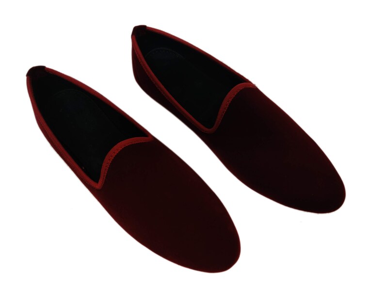 May include: A pair of burgundy velvet loafers. These slip-on shoes have a classic design with a rounded toe and a low profile. They feature a red trim around the opening and a black interior. Suitable for formal or casual wear.