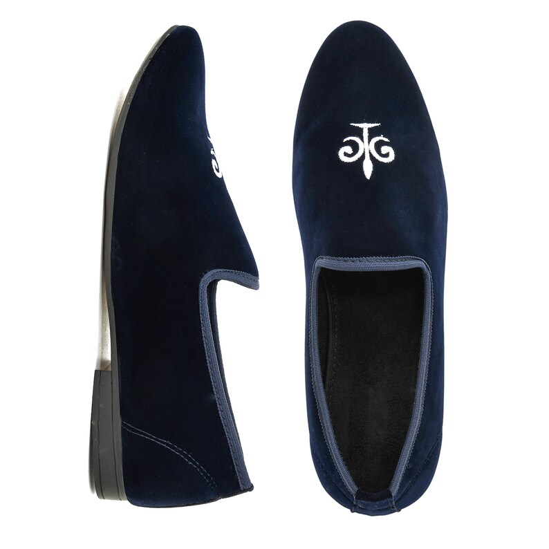 May include: A pair of navy blue velvet loafers with white embroidered detailing. The shoes have a rounded toe and a low heel. The design is on the top and side of the shoe.