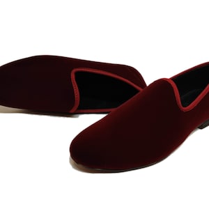 May include: Burgundy velvet loafers with red trim. These slip-on shoes have a classic design and a low heel. The interior is black. Suitable for formal or casual wear. The shoes are made of a soft, luxurious material.