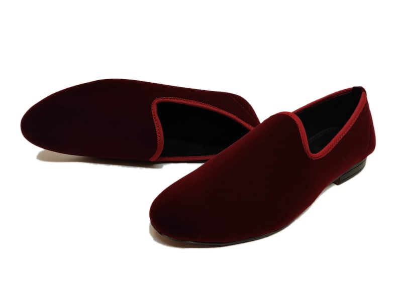 May include: Burgundy velvet loafers with red trim. These slip-on shoes have a classic design and a low heel. The interior is black. Suitable for formal or casual wear. The shoes are made of a soft, luxurious material.