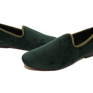 May include: A pair of dark green velvet loafers with a light green trim around the top edge. The loafers have a pointed toe and a low heel.
