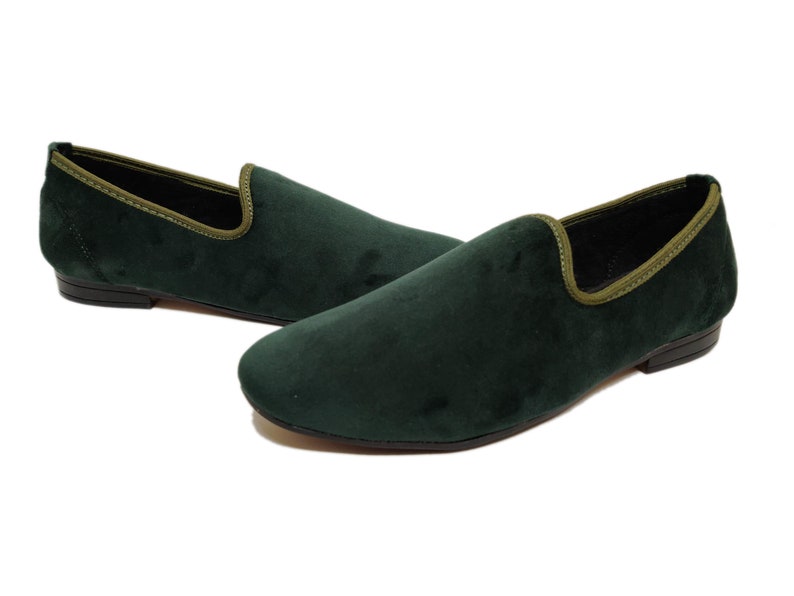 May include: A pair of dark green velvet loafers with a light green trim around the top edge. The loafers have a pointed toe and a low heel.