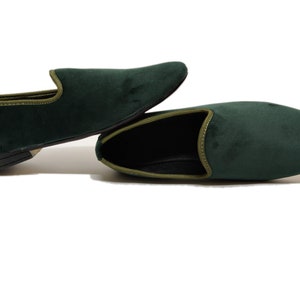 May include: A pair of dark green velvet loafers with a light green trim. The loafers are laid out on a white surface.