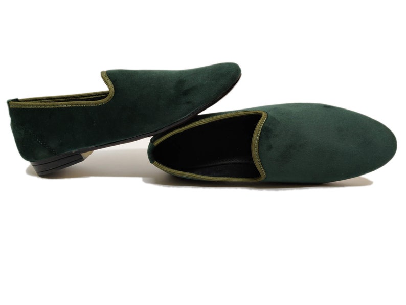 May include: A pair of dark green velvet loafers with a light green trim. The loafers are laid out on a white surface.