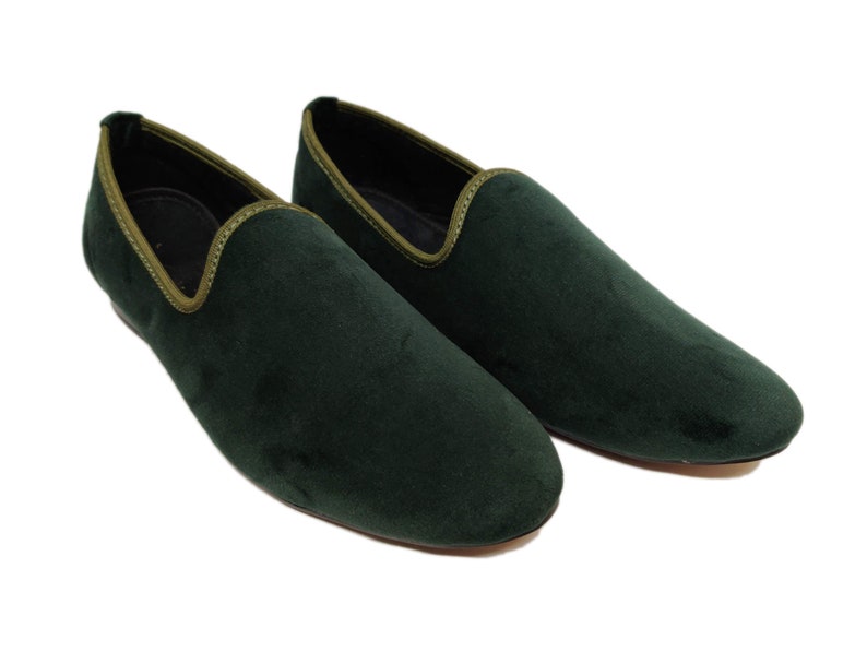 May include: A pair of dark green velvet loafers with a light green trim around the edge.